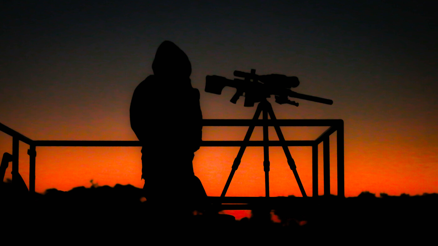 Marksman behind a scoped rifle at sunset